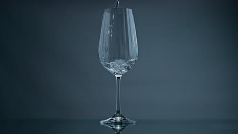 water pouring wine glass at dark background closeup. clear liquid splashing