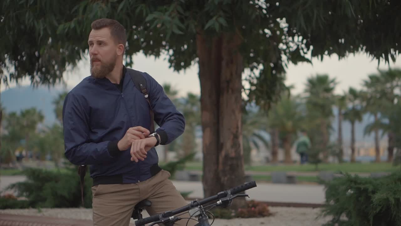 Man checking time on his smartwatch while sitting next to a bicycle in a park