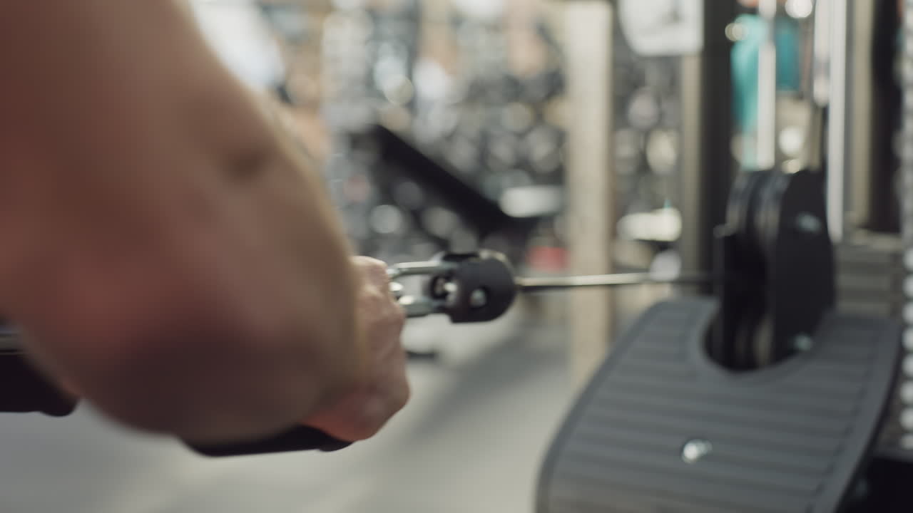 Athlete hand grips weight machine handle and pulls with controlled motion, highlighting muscle tension and strength during repetitive training in modern gym setting with blurred background activity