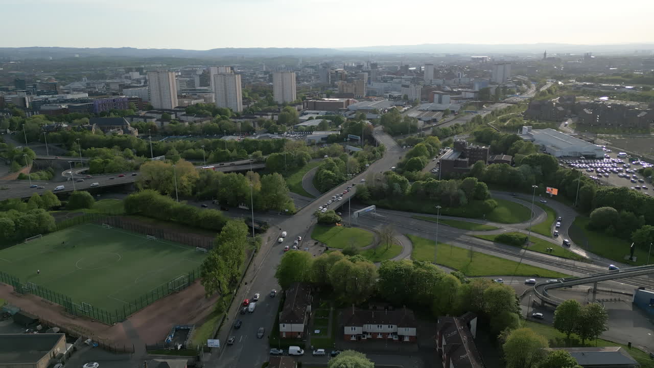 Ripresa aerea dall'alto con drone che mostra un intenso flusso di traffico sulle strade urbane e sugli svincoli autostradali con lo skyline della città di Glasgow in lontananza