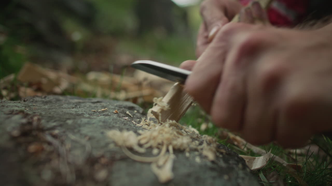 Hands of Man Making Feather Sticks with Knife to Start Fire in Wilderness