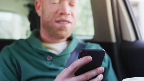 hombre afroamericano albino feliz con rastas sentado en el coche usando un teléfono inteligente