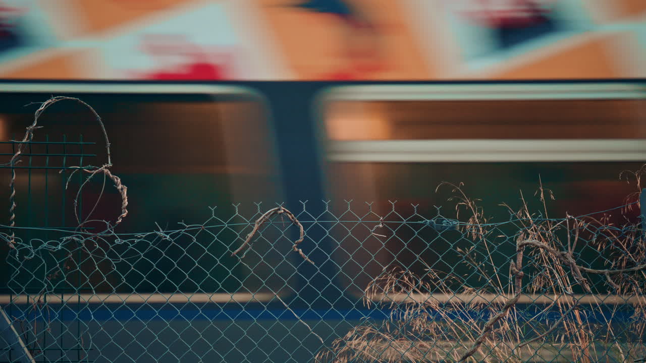 A fast moving train creates a colorful horizontal blur while a piece of rusted wire fencing sits still in the bottom corner