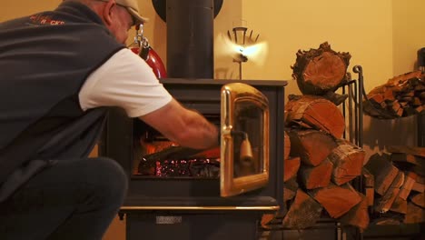 Putting-log-in-woodstove-with-logs-in-background