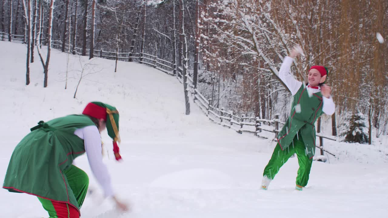 Santa Claus elves play snowballs on a snowy field against the background of the forest