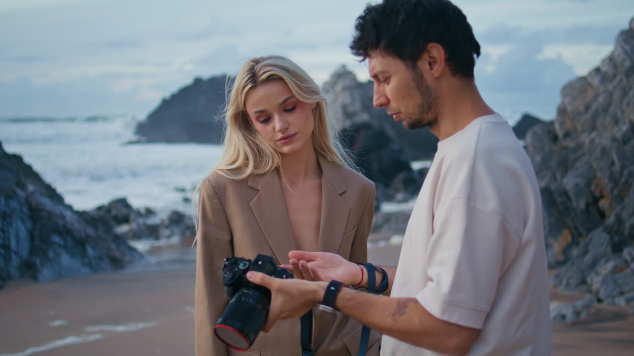 사진가가가 해안 근접에서 모델 사진을 논의하고 있습니다. 촬영 팀이 일하고 있습니다.