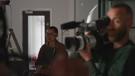 female film director working on set shooting movie or video in studio with cameraman sound recordist in foreground