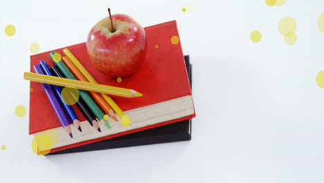 animation of yellow spots over apple and colour pencils on stack of books