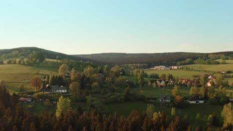 drone shot of czech highlands village surrounded with forest during sunset