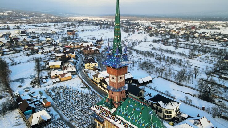 Vue aérienne par drone du cimetière joyeux de Sapanta en hiver, Roumanie. Plusieurs pierres tombales, église, neige
