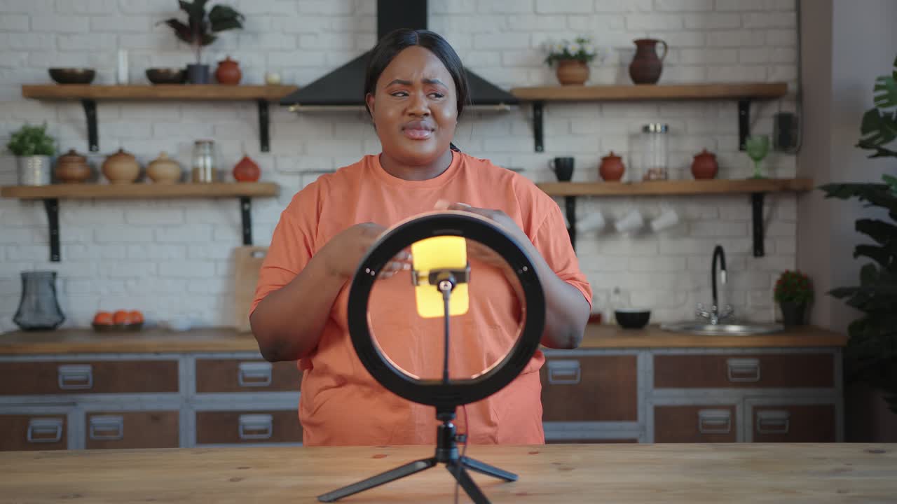 Plump blogger with ponytail speaks at tripod with smartphone