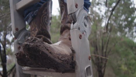 Man-standing-on-ladder-with-muddy-cowboy-boots-on-ranch-farm