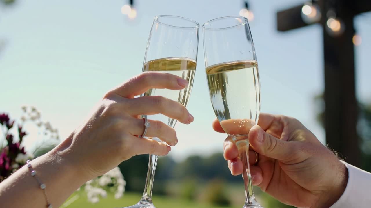 Pareja entrando desde los lados, brindando con copas de champán en el jardín, mostrando anillo y puño de camisa