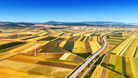 wind turbines in open fields. vibrant fields with varying colors stretch across the landscape, scattered with wind turbines under a clear blue sky