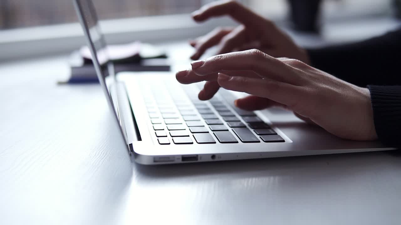 Unrecognizable female hands with accurate manicure typing something on laptop keyboard