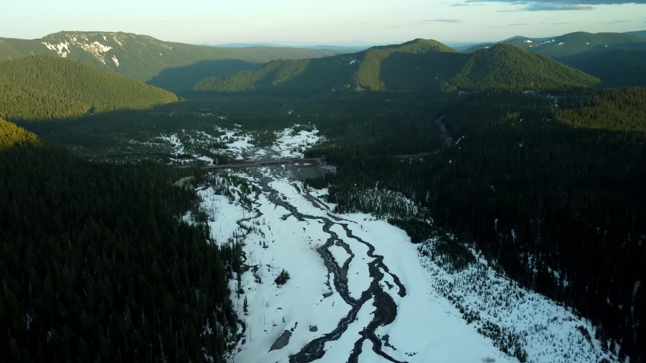 US, Oregon, Mt Hood, White River, 2025-04-22 - Drone view of the White River near Mt Hood in spring, with snow still covering the creek and trees with the highway bridge in the center