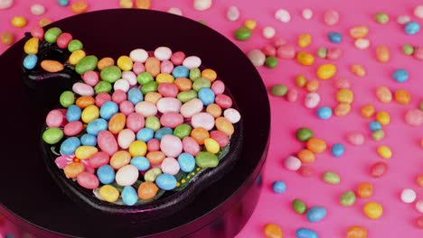 pile of many round chewy candies dragee in multicolored glaze rotate slowly on turntable. with pink light.