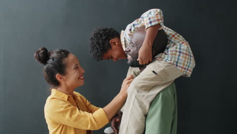 happy african american man holding little son on shoulders and talking with wife