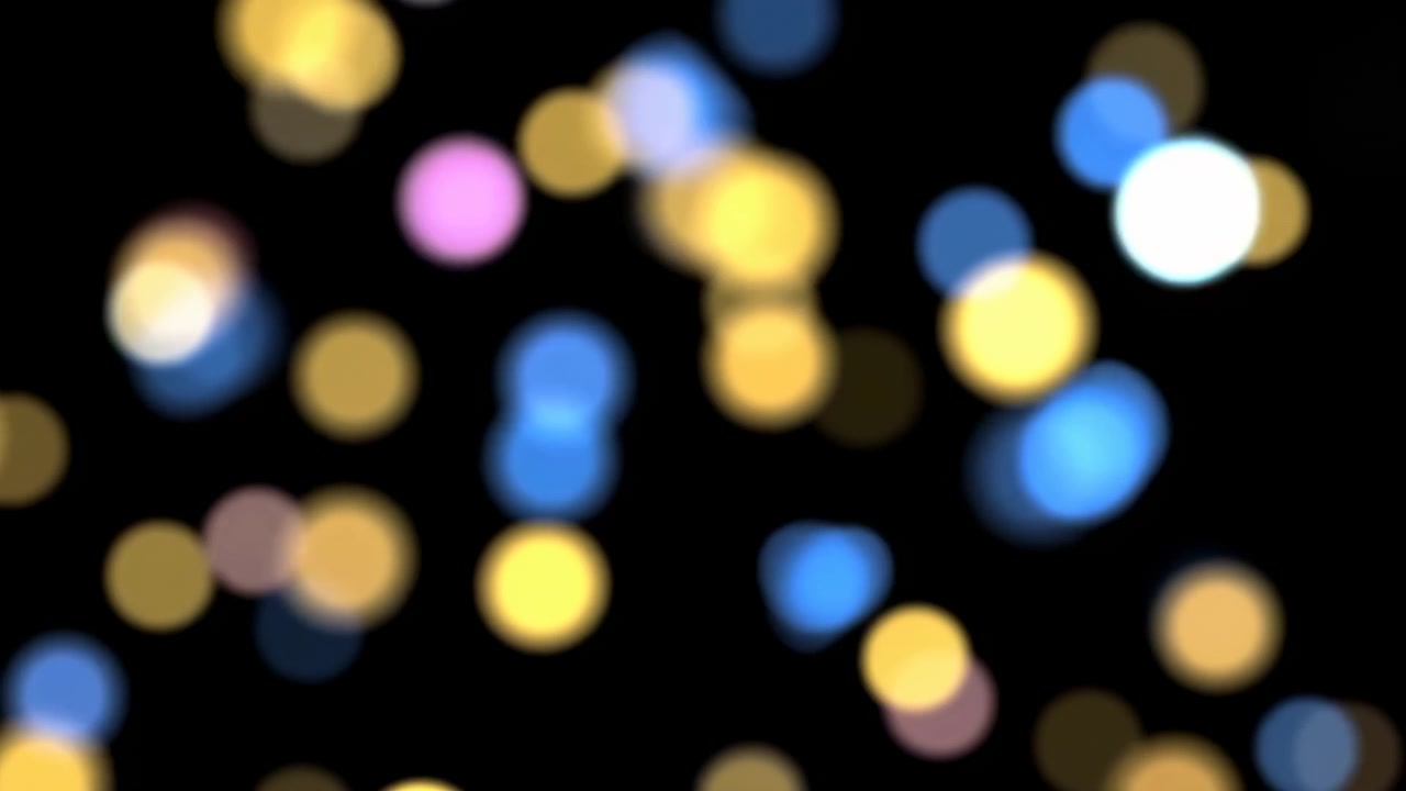 Punti bokeh morbidi su nero, riflessi circolari multicolori fluttuano su uno sfondo profondo creando un'atmosfera calda e festosa.