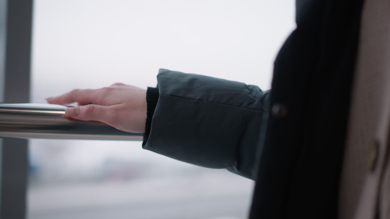 검은색 후디를 입은 소녀의 손과 반지로 장식된 손가락이 매끄러운 금속 레일에 미끄러져 걸어가는 클로즈업, 흐릿한 배경으로 부드럽고 현대적이고 세련된 분위기를 만니다.