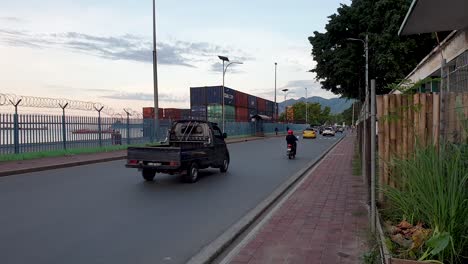 City traffic commuting, cars, taxi and motorbikes driving along the dock waterfront with barbed wire fence in background in Southeast Asian city