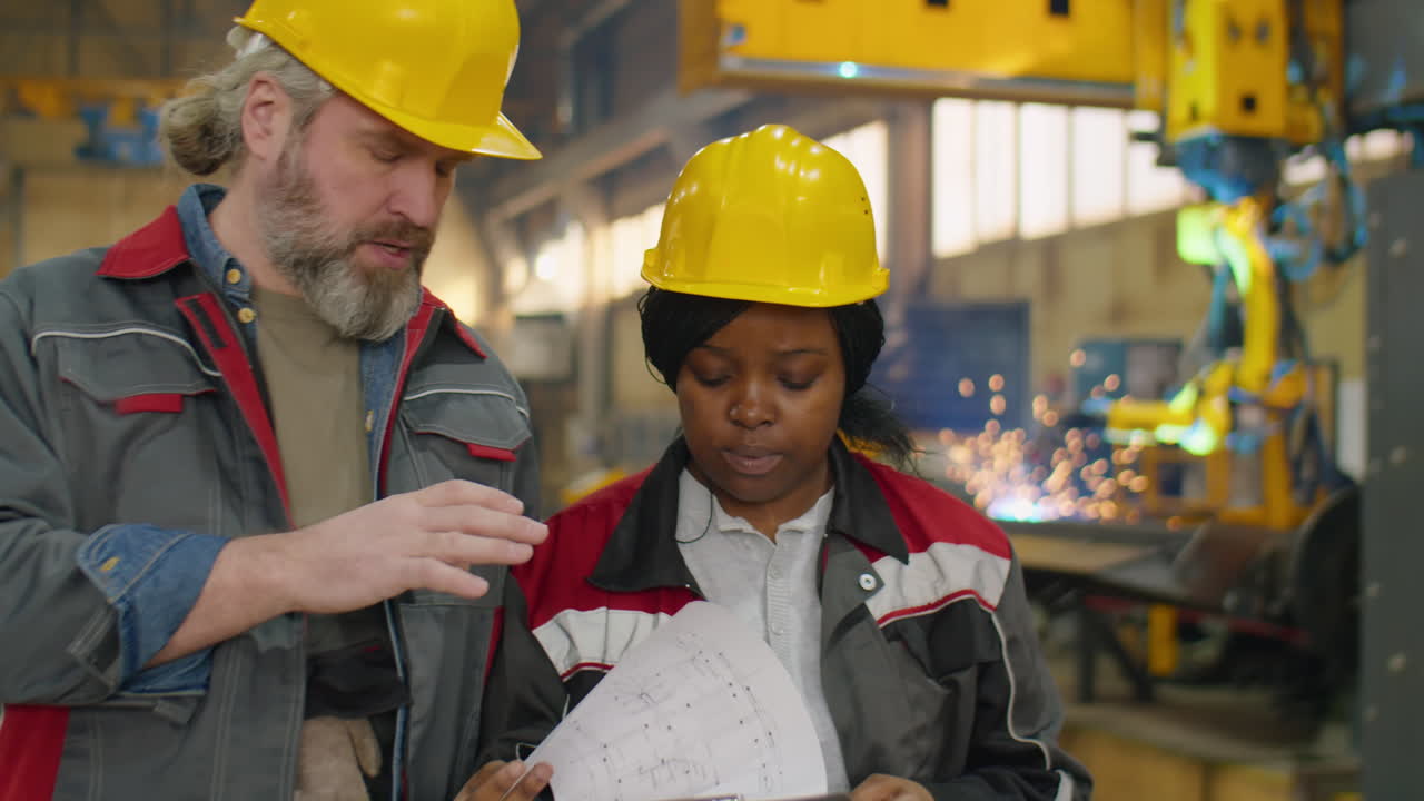 Diverse Coworkers in Hardhats Walking and Speaking in Machinery Plant