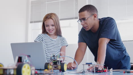 female student with teacher building robot vehicle in after school computer coding class