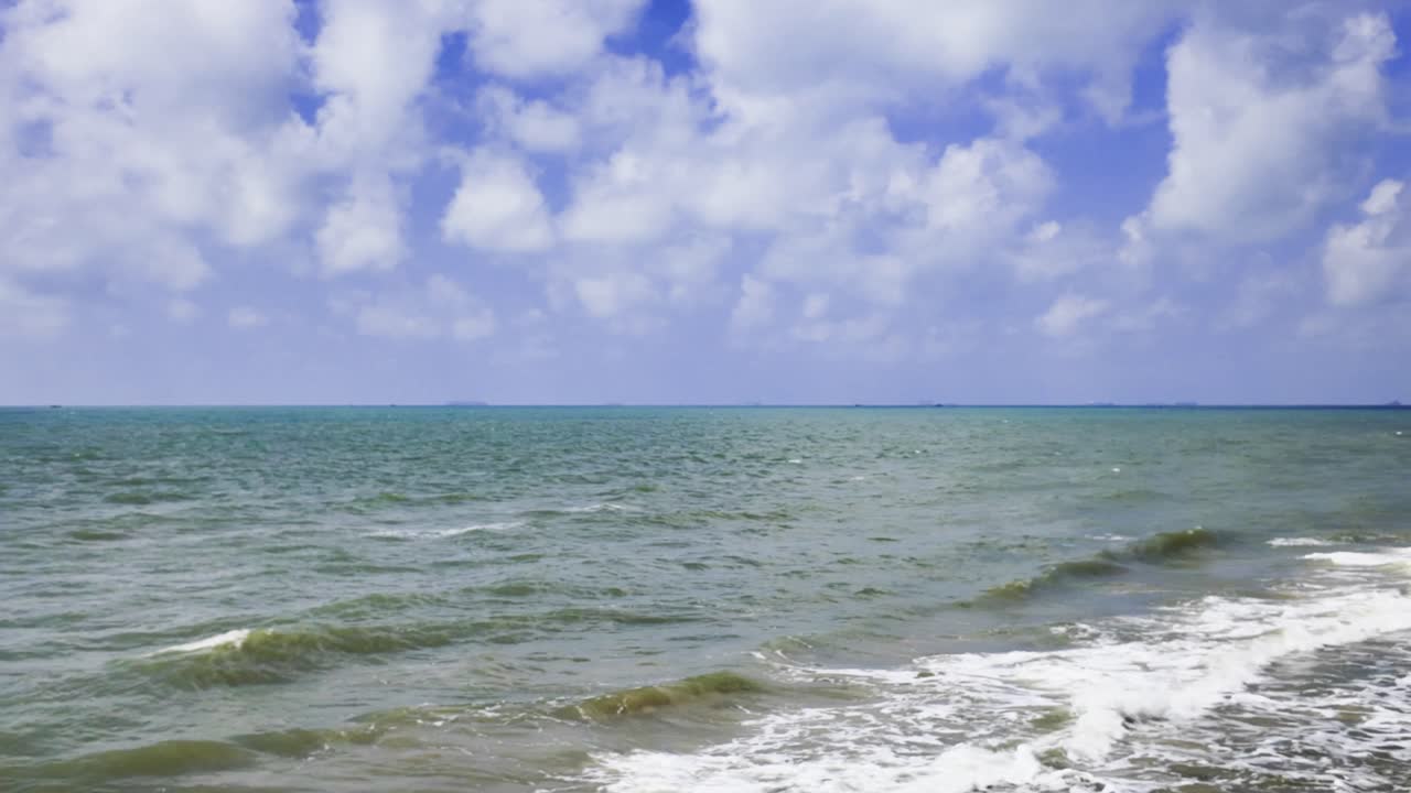 Passeggiando lungo Bai Tam Nong Noc a Vung Tau, Vietnam, si vedono le onde che si infrangono sulla riva. Il cielo è blu con nuvole. Le persone si godono la spiaggia e l'atmosfera marina.