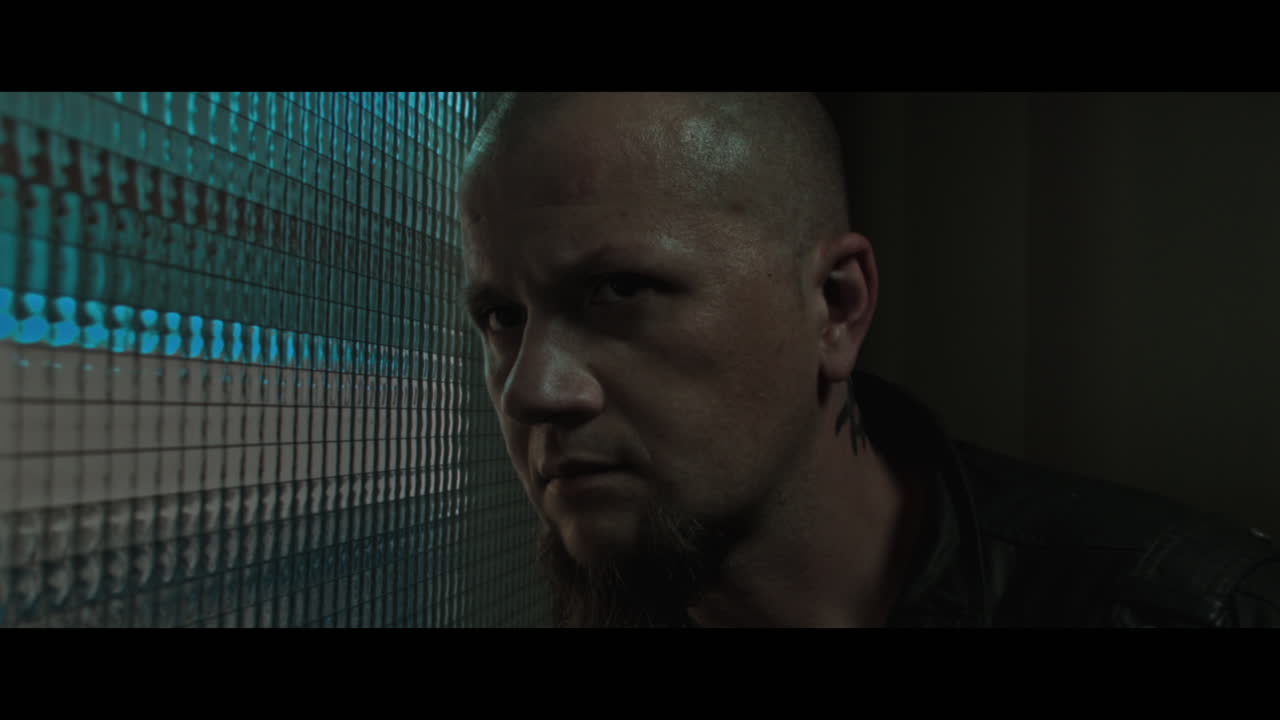 A bald dangerous looking man checks the corridor through reinforced glass