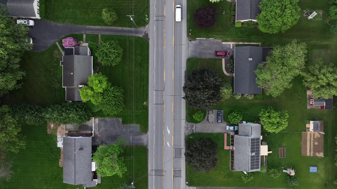 Suburb neighborhood with single Family houses and driveways in spring. Aerial top down flyover. Solar panels on roof of buildings. Cloudy day in calm suburb district of town. Driving cars on street.
