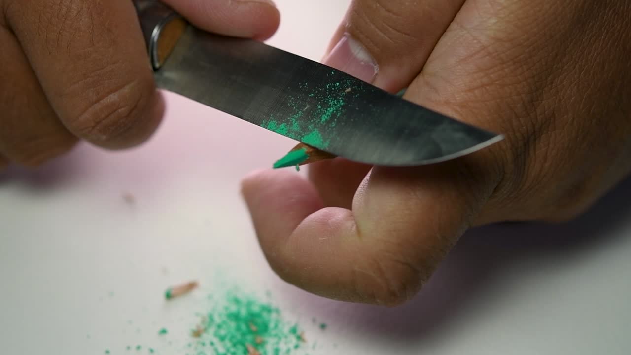 날카로운 칼로 연필과 색연필을 천천히 갈고 있는 손의 영상