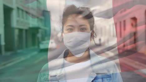 Animation-of-flag-of-italy-waving-over-woman-wearing-face-mask-during-covid-19-pandemic