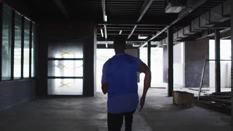 african american man wearing sports clothing jogging through an empty urban building