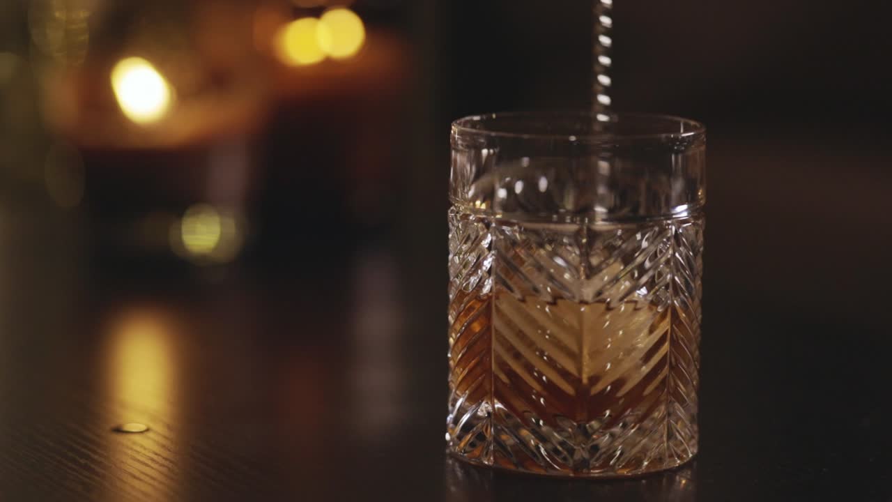 Barman mezclando el whisky con cubitos de hielo usando una cuchara de bar. Primer plano.