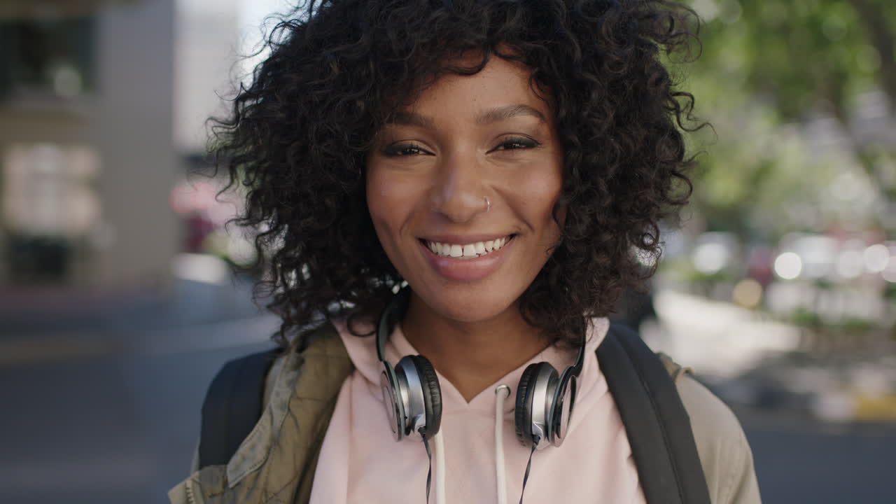 ritratto di giovane attraente donna afroamericana afro acconciatura sorridente allegro in strada della città indossando cuffie
