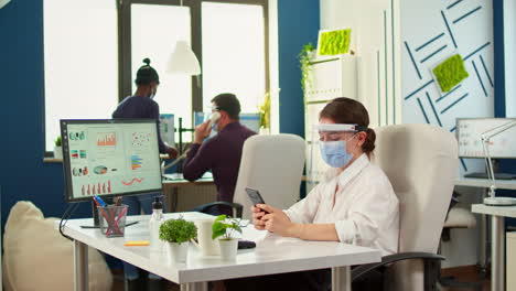 Businesswoman-with-mask-chatting-using-phone-in-office-room