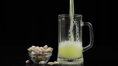 la cerveza se vierte en el vidrio sobre un fondo negro. cuenco de pistachos