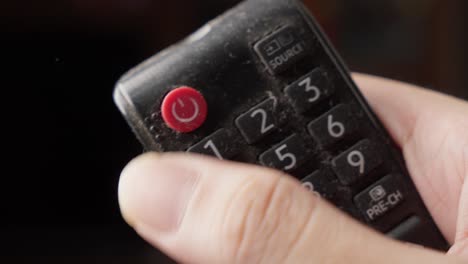 holding tv remote control and pressing on-off red button by thumb, close up