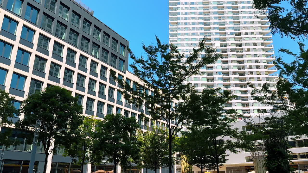 Urban park with buildings nearby. Lush green grass and trees surround contemporary buildings under a bright blue sky, showcasing urban life and nature