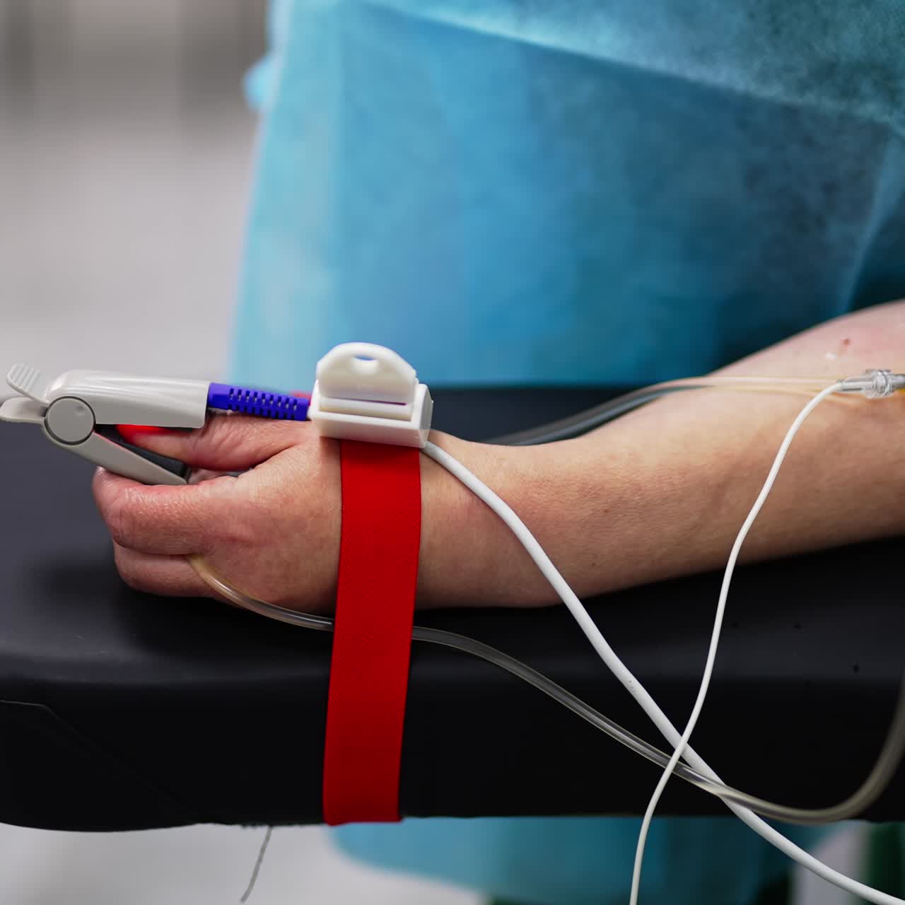 An arm of an adult patient connected to diverse equipment in surgery theatre. Close up. Blurred backdrop