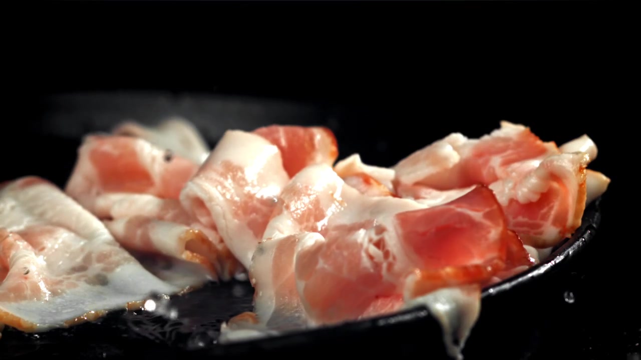 Fette di pancetta cruda che cadono in una padella calda al rallentatore