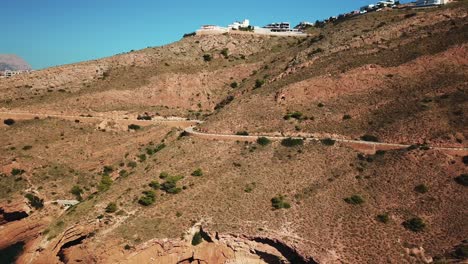 Vista-Aérea-Hacia-Atrás-En-Cámara-Lenta-De-Un-Camino-Claro-Que-Conecta-La-Montaña-Y-El-Mar-Sin-Vehículos-Ni-Personas-Para-Caminar-En-La-Hermosa-Ciudad-De-Benidorm-En-España