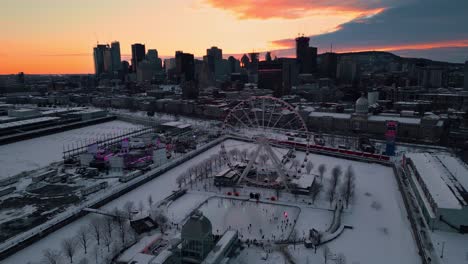 aerial shot around montreal ferris wheel and the old port at sunset during winter with the ice skating ring in the foreground, montreal city, quebec region, canada