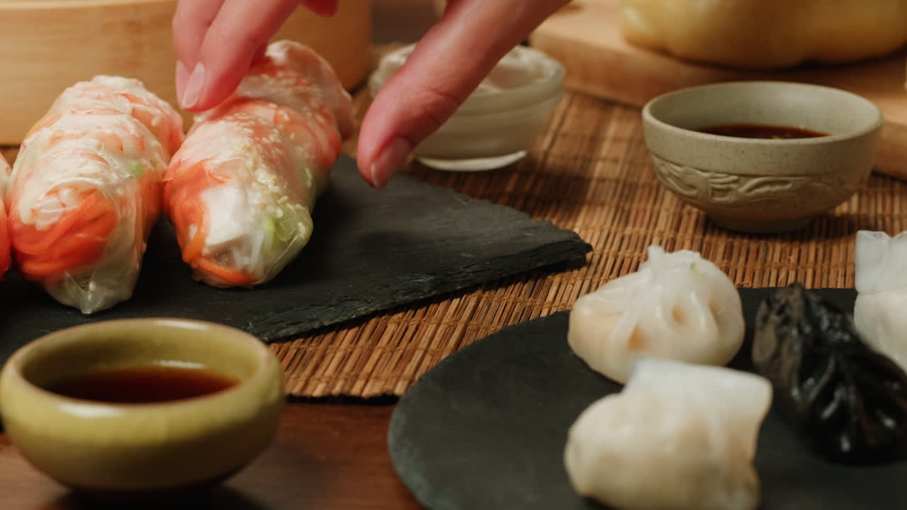 Hand Picking Up a Fresh Spring Roll from a Plate of Asian Food