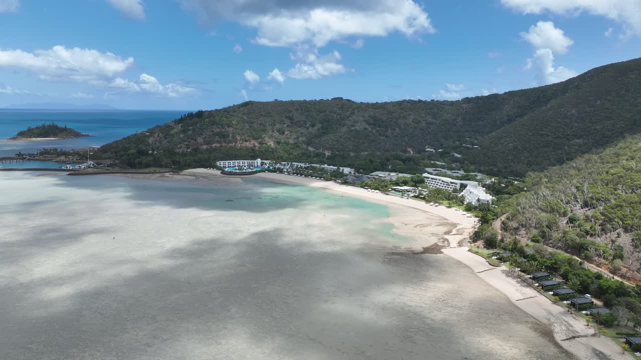 日中のドローン静止画。ヘイマン島の浅い湾の干潟、湾曲した砂浜、緑の丘に囲まれたリゾートのワイドビュー。ウィットサンデー諸島、クイーンズランド州、オーストラリア。
