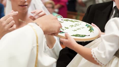 bride with white dress unlacing ribbon taking out wedding ring from little bridesmaid