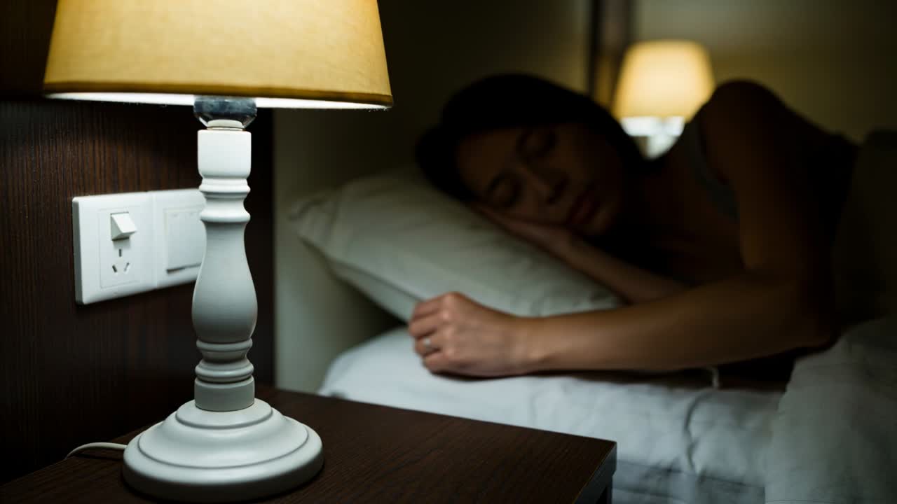 Træt kvinde i camisole rækker ud og trykker på vægkontakten ved lampen i soveværelset, liggende på pude
