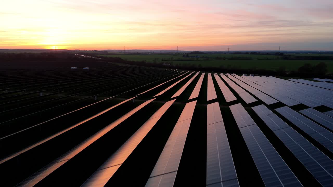 Droneoptagelse i stor højde af infrastruktur for vedvarende energi nær Newmarket England under en kold vinter solnedgang med røde lysrefleksioner på solarglas