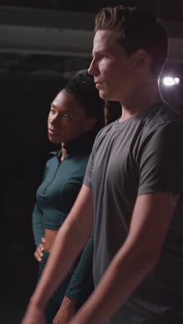 vertical video portrait of determined male and female athletes in in fitness clothing shot in gym with low key lighting