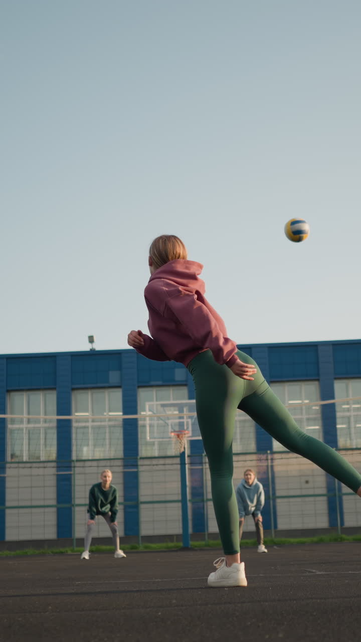 뒷면에는 두 명의 여성이 배경에서 지켜보고 있으며, 건물 뒤에는 공을 잡기 위해 서두르는 파란색의 여자가 있습니다.